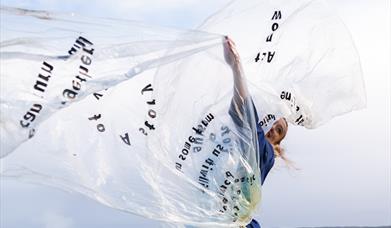 A dancer spinning with a large sheet of clear plastic.