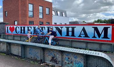 Cyclists in front of a Cheltenham sign