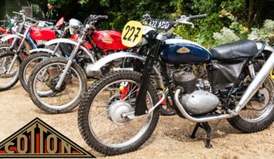 A line of vintage motorcycles parked in the Folk of Gloucester courtyard with the Cotton logo in one corner