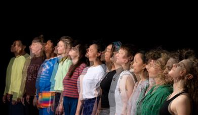 11 people stood in a row against a black backdrop.