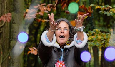 A woman standing in a forest and throwing multicoloured orbs in the air with a joyful expression on her face