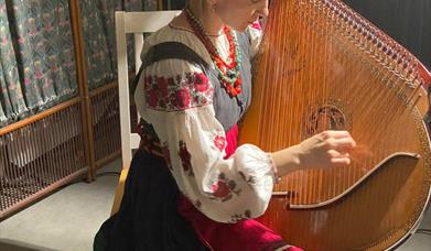 A woman in traditional Ukrainian dress playing a large round wooden instrument with lots of strings