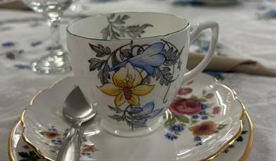 A white China tea cup with blue patterns sitting on a matching saucer on a table with a white embroidered tablecloth