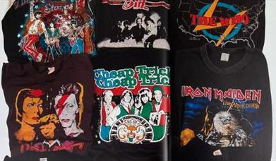 A pile of t shirts with different band logos including David Bowie, The Who and The Rolling Stones