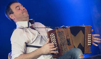 A man energetically playing melodeon on stage