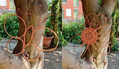 A woven wicker flower and a woven wicker butterfly in a tree in The Folk of Gloucester garden