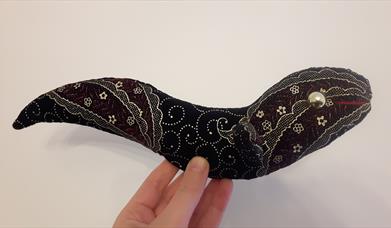 A hand sewn cuddly toy eel made from black velvet with gold paisley patterns and gold button eyes