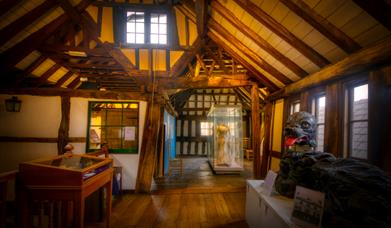 The interior of The Folk of Gloucester's historic Tudor building showing its timber framed ceiling, wattle and daub walls and cabinets with various hi