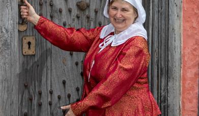 A guide dressed as a 17th century woman opening an old wooden front door.