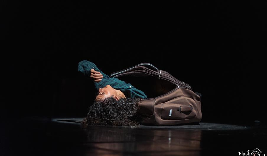 A circus performer half out of a suitcase on stage.