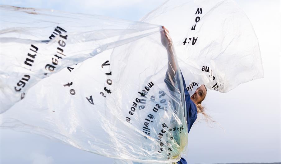 A dancer spinning with a large sheet of clear plastic.