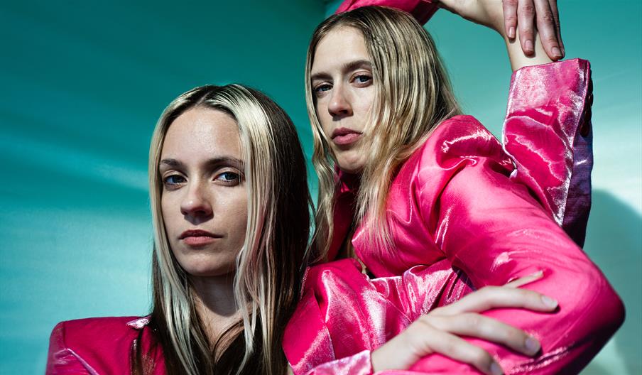 Two dancers wearing bright pink suits with their arms intertwined.