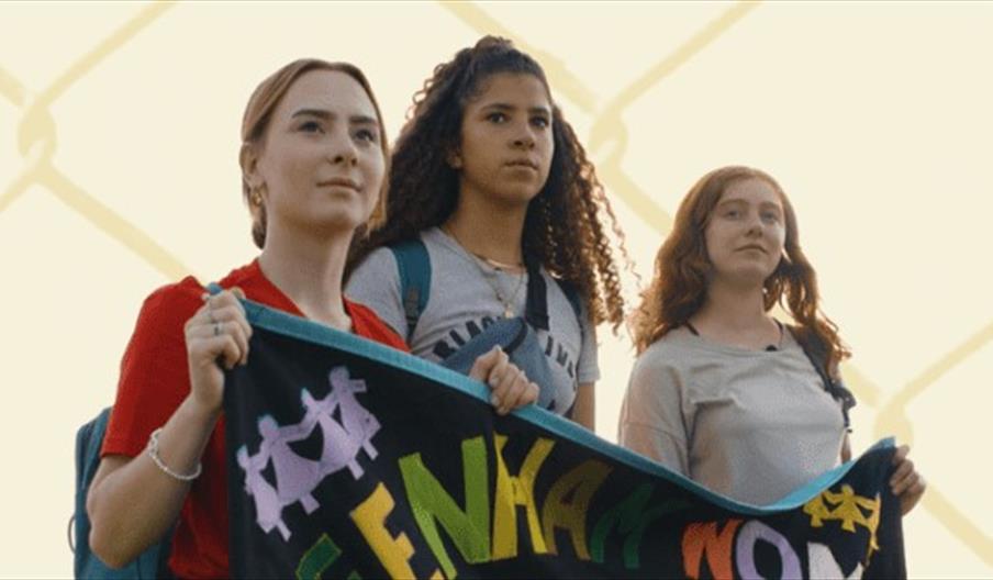 Three young women holding a fabric banner with colourful lettering sewn onto it