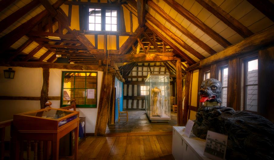 The interior of The Folk of Gloucester's historic Tudor building showing its timber framed ceiling, wattle and daub walls and cabinets with various hi