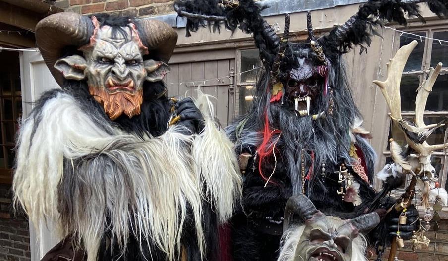 Two adults and a child in fur outfits and horned masks with bared teeth