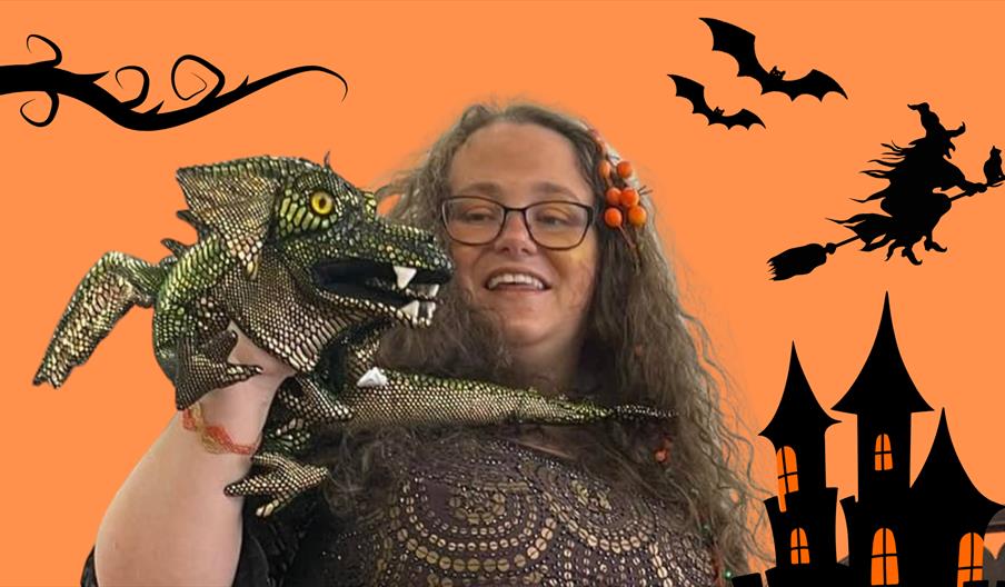 A smiling woman with a dragon puppet against an orange background with drawn silhouettes of a castle, flying witch and some bats.