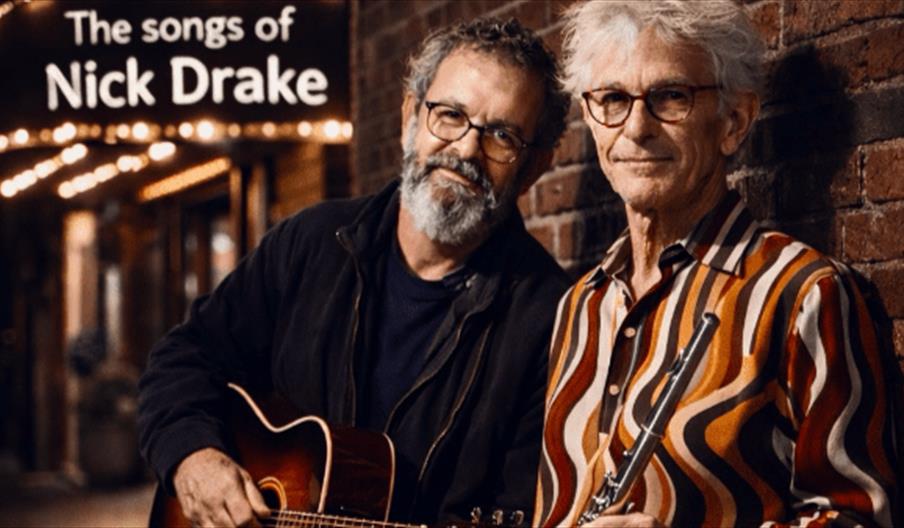 A man with glasses and dark grey hair and beard holding an acoustic guitar and a man with windswept light grey hair holding a flute in a street outsid