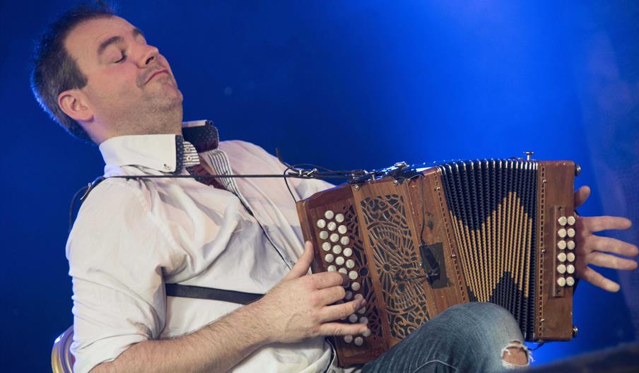 A man energetically playing melodeon on stage