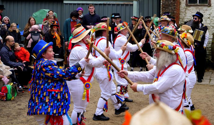 A group of Morris dancers in white outfits with bells and sticks dancing in front of a crowd of people in winter outdoors