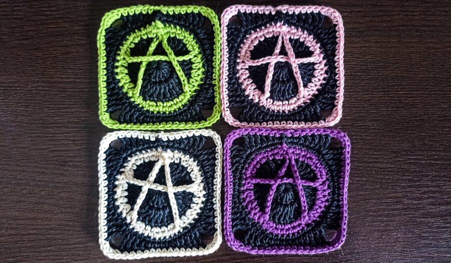 Four crocheted "granny squares" with the anarchy symbol sewn into them