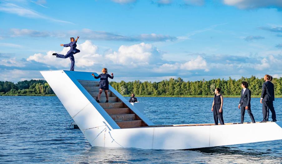 Dancers on a white staircase floating on water.