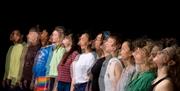11 people stood in a row against a black backdrop.