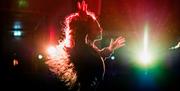 A performer dancing on stage, backlit by colourful lights.