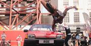 A performer jumping over a spinning red car.