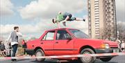 A performer jumping over a spinning red car.