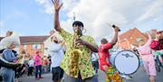 A musician in the parade wearing brightly coloured patterned shirt  and playing a saxophone, surrounded by other musicians and dancers