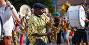A musician wearing a brightly patterned shirt, playing a saxophone as part of the street parade