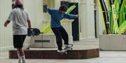 A skateboarder performs a trick on a skateable sculpture made of wood and metal on an urban street, showcasing skill and style amidst vibrant surround