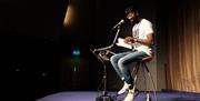 Inua on stage reading poetry into a microphone.
