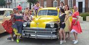 A group of women dressed for the Gloucester Goes Retro Festival, posing with an old car.
