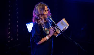 Hollie McNish stood in front of a microphone on stage with a book in her hand